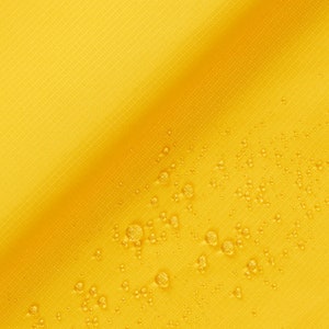 May include: A close-up of a yellow fabric with a diagonal line. The fabric has a textured surface and is covered in small water droplets.