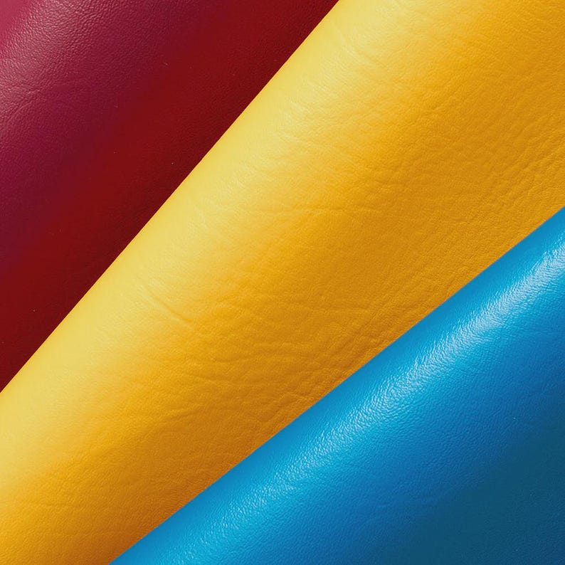 Puede incluir: Primer plano de cuatro rollos de cuero de colores. Los colores son un borgo&ntilde;a profundo, un rojo brillante, un amarillo soleado y un azul vibrante. El cuero tiene una superficie texturizada.