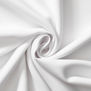 May include: A close-up shot of white fabric with a ribbed texture. The fabric is arranged in soft folds and curves, creating a swirling pattern. The material appears smooth and opaque, with subtle highlights and shadows.
