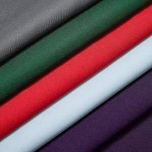 Könnte beinhalten: Diagonale Ansicht von Stoffmustern in verschiedenen Farben. Die Farben umfassen Grau, Waldgrün, Rot, Hellblau und Lila. Der Stoff hat eine subtile Textur und scheint ein mittelschweres Material zu sein, das für Kleidung oder Heimdekoration geeignet ist.