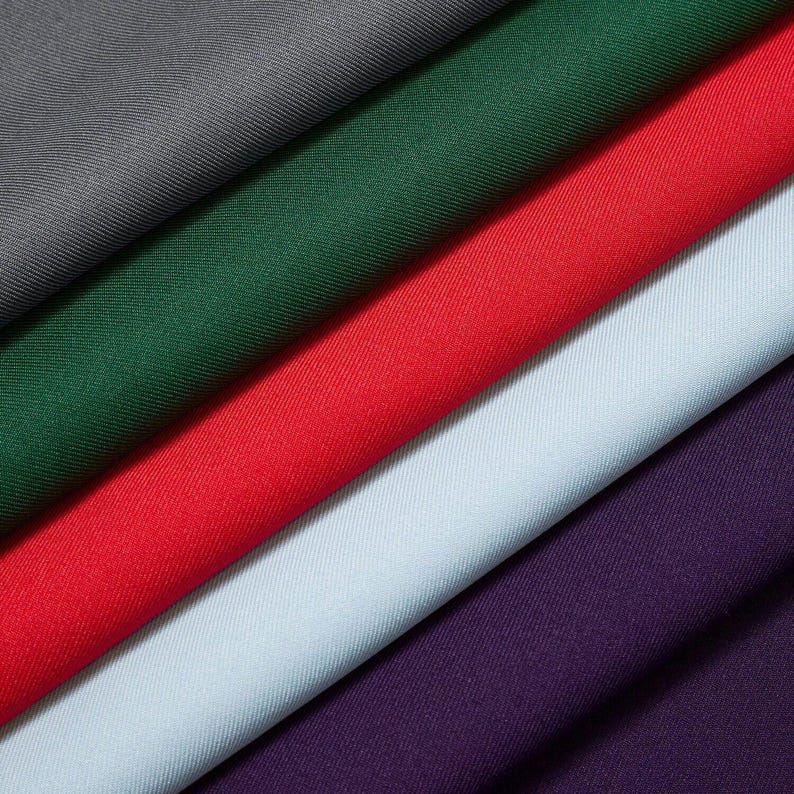 Puede incluir: Vista diagonal de varias muestras de tela en varios colores. Los colores incluyen gris, verde bosque, rojo, azul claro y morado. La tela tiene una textura sutil y parece ser un material de peso medio, adecuado para ropa o decoraci&oacute;n del hogar.