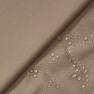 May include: A close-up of two pieces of fabric, one brown and one beige. The beige fabric has water droplets on it, showing that it is water-resistant.