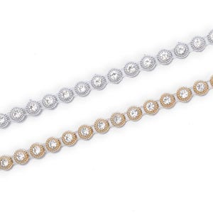 May include: Two decorative rhinestone trims. One trim is silver with clear rhinestones, and the other is gold with clear rhinestones. The rhinestones are set in a circular pattern. The trims are on a white background.