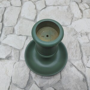 May include: A green wooden candlestick holder. It has a circular base and a cylindrical top. The inside of the top is natural wood. The holder is painted in a matte green finish.