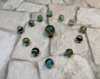 Könnte beinhalten: Eine Sammlung von 12 bunten Glasmurmeln mit grünen, blauen, roten und weißen Spiralen. Die Murmeln sind in Sternform auf einer grauen Steinoberfläche angeordnet.