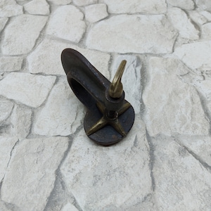 May include: A vintage-style, dark metal clamp with a brass screw and a star-shaped base. The clamp is designed to hold objects. The brass screw is used to tighten the clamp. The item is likely used for woodworking or crafts.
