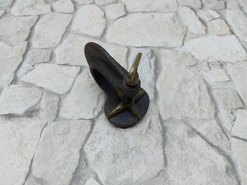 May include: A vintage-style, dark metal clamp with a brass screw and a star-shaped base. The clamp is designed to hold objects. The brass screw is used to tighten the clamp. The item is likely used for woodworking or crafts.