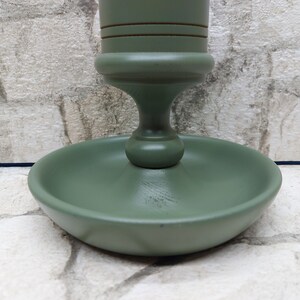 May include: A sage green wooden candlestick holder with a round base and a decorative stem. The candlestick holder has a classic design and is painted in a matte finish. The base measures approximately 10 cm in diameter.