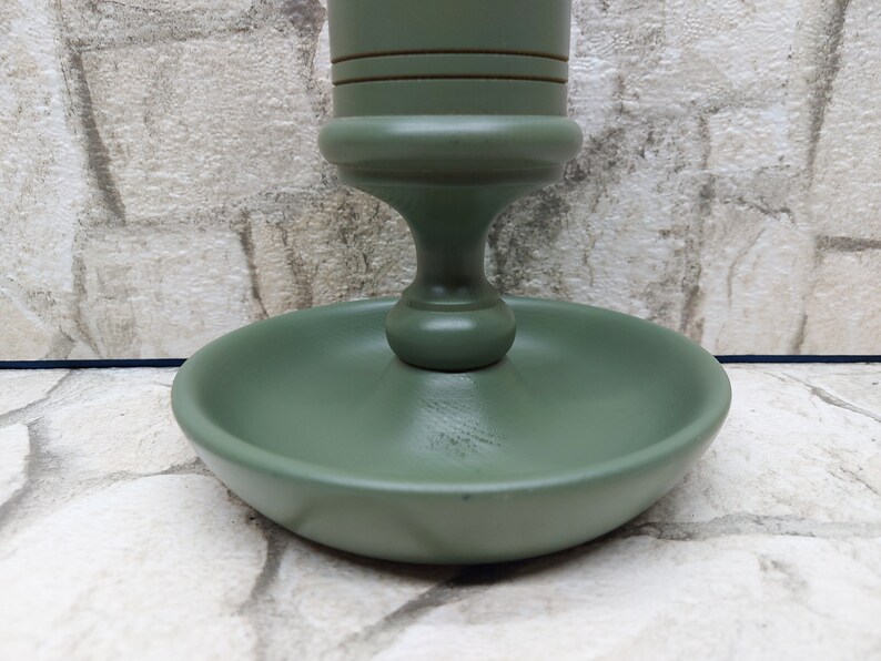 May include: A sage green wooden candlestick holder with a round base and a decorative stem. The candlestick holder has a classic design and is painted in a matte finish. The base measures approximately 10 cm in diameter.