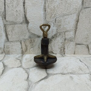 May include: A vintage metal clamp with a brass handle and screw mechanism. The clamp has a dark, aged appearance, with a star-shaped base and a threaded rod. The handle is a loop shape.