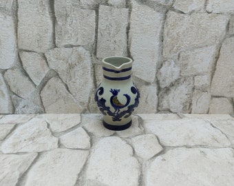 Puede incluir: Una jarra de cerámica con cuerpo beige claro y diseño decorativo azul oscuro. La jarra presenta un motivo de pájaro y rayas azules alrededor de la parte superior. La jarra se utiliza probablemente para servir bebidas.