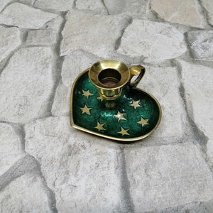 May include: A heart-shaped candle holder with a green enamel finish and gold star accents. The candle holder has a brass candle cup and a small handle. The base is approximately 4 inches wide.