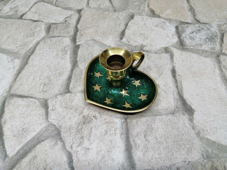 May include: A heart-shaped candle holder with a green enamel finish and gold star accents. The candle holder has a brass candle cup and a small handle. The base is approximately 4 inches wide.