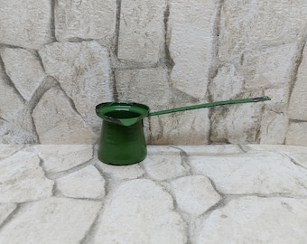 May include: A small green metal coffee pot with a long handle. The pot is sitting on a white stone surface.