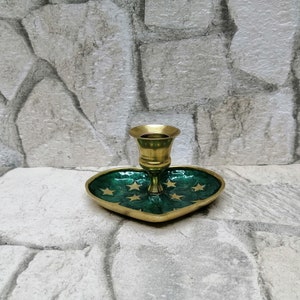 May include: A brass candlestick holder with a heart-shaped base. The base is green with gold stars and a gold border. The candlestick holder is made of brass.