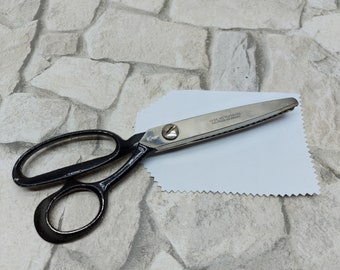 May include: A pair of black-handled scissors with a silver blade, resting on a white fabric. The scissors have the text "CARL WEYERSBERG SOLINGEN GERMANY" printed on the blade. The scissors are designed for cutting fabric.