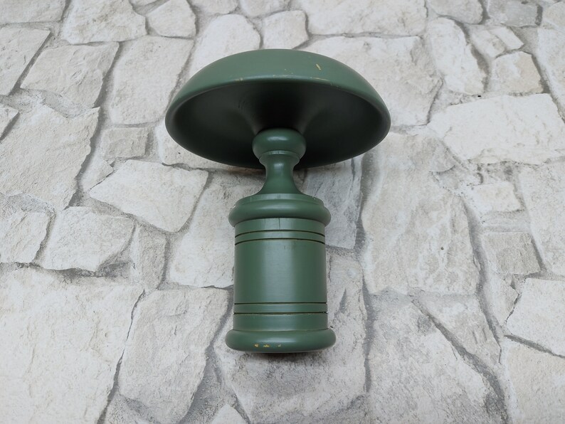 May include: A green wooden decorative object with a mushroom-shaped top and a cylindrical base. The object is painted in a solid green colour and has a classic, vintage design. The object is likely a decorative item or a small table.
