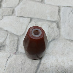 K&ouml;nnte beinhalten: Ein facettierter, rotbrauner Flaschenverschluss mit wei&szlig;em Innenraum. Der Verschluss hat eine geometrische Form und ist f&uuml;r eine Flasche konzipiert. Das Produkt ist wahrscheinlich f&uuml;r Wein oder andere Getr&auml;nke.