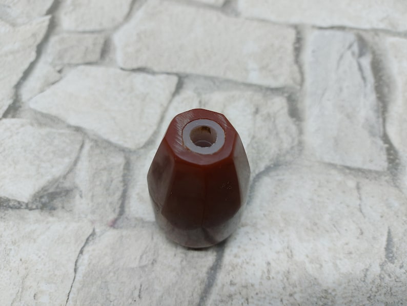 K&ouml;nnte beinhalten: Ein facettierter, rotbrauner Flaschenverschluss mit wei&szlig;em Innenraum. Der Verschluss hat eine geometrische Form und ist f&uuml;r eine Flasche konzipiert. Das Produkt ist wahrscheinlich f&uuml;r Wein oder andere Getr&auml;nke.