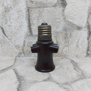 Puede incluir: Un portalámparas vintage marrón y latón con un diseño multipuerto. El portalámparas tiene una parte superior roscada para la fijación de la bombilla y múltiples puertos laterales. La base es de color marrón oscuro y la parte superior es de latón.