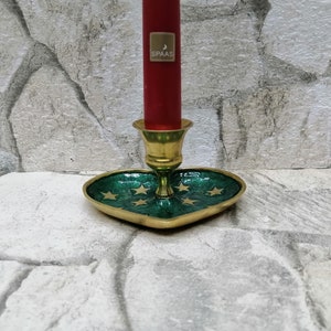 May include: A brass candle holder with a heart-shaped green base adorned with gold stars. A red candle with a gold label is inserted into the holder. The candle holder is a decorative item.