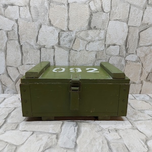 May include: An olive green wooden box with a hinged lid and metal clasp. The top of the box has the number "032" stenciled in white. The box has two wooden handles on the top and is sitting on a stone surface.
