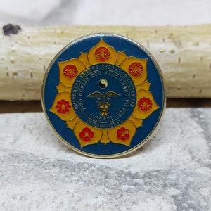 May include: A round, blue and gold pin with the text "UNIVERSAL RESEARCH INSTITUTE" and other text. The pin features a flower design with red and gold accents, and a caduceus symbol.