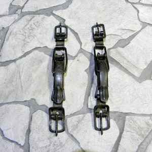 May include: Two black metal buckles with a simple design. The buckles are on a white stone background.