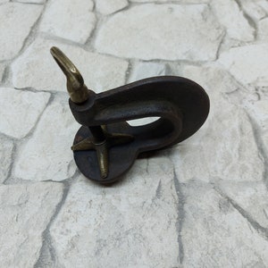 May include: A vintage-style, dark metal object with a circular base and a curved, open design. It features a brass-colored loop and a star-shaped support. The object appears to be an antique tool or decorative piece.