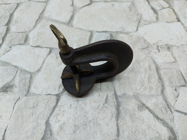 May include: A vintage-style, dark metal object with a circular base and a curved, open design. It features a brass-colored loop and a star-shaped support. The object appears to be an antique tool or decorative piece.