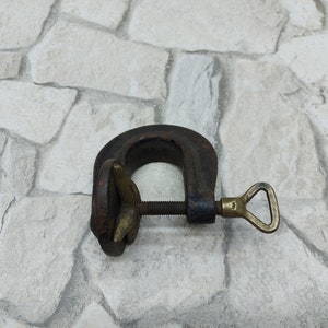 May include: A vintage C-clamp, made of dark metal with a brass screw and handle. The clamp is designed to hold objects together and is commonly used in woodworking and metalworking projects.