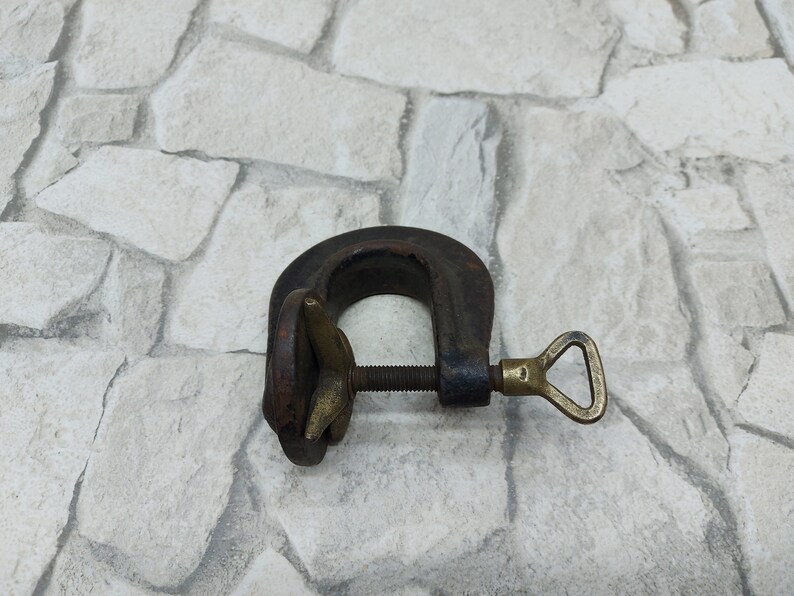 May include: A vintage C-clamp, made of dark metal with a brass screw and handle. The clamp is designed to hold objects together and is commonly used in woodworking and metalworking projects.