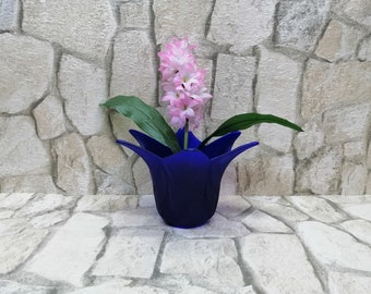 May include: A blue ceramic vase with a unique tulip shape holds a pink hyacinth flower arrangement. The vase is sitting on a stone surface.