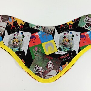 Può includere: Un bandana di stoffa nero con un bordo giallo. Il bandana è stampato con un collage di copertine di album dei Queen con Freddie Mercury e altri membri della band.