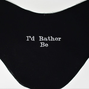 Può includere: Tessuto nero con un messaggio ricamato in bianco che dice "I'd Rather Be".