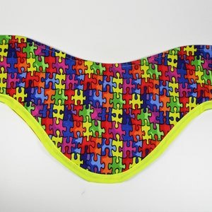 Può includere: Un foulard da collo colorato con un motivo a puzzle e un bordo giallo brillante.