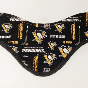 Può includere: Scaldacollo in tessuto nero e giallo a tema Pittsburgh Penguins. Il tessuto presenta il logo della squadra, mazze da hockey e le parole "PITTSBURGH PENGUINS" e "#1 TEAM". Lo scaldacollo è bordato con tessuto nero.