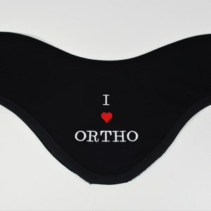 Può includere: Bandana di cotone nero con ricamo bianco che dice "I ♥ ORTHO".