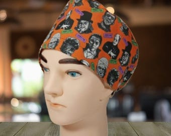 May include: Orange and black scrub hat with a print of various horror movie characters. The hat has a black brim and a white elastic band.