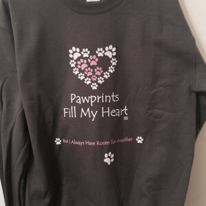 May include: Dark gray sweatshirt with the text "Pawprints Fill My Heart" and paw print graphics in white and pink. The design includes a heart shape made of white paw prints, with pink paw prints inside.