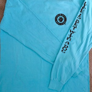 May include: A light blue long-sleeve shirt with the text "Life is Best With a Dog" printed in black on the sleeve and a paw print design on the chest. The shirt is made of a soft material.