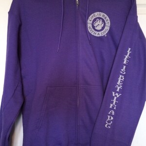 May include: A purple zip-up hoodie with a drawstring hood and front pockets. The left sleeve has the text "LIFE IS BEST WITH A DOG" printed vertically. The chest features a circular design with a paw print and the words "LIFE IS BEST WITH A DOG".