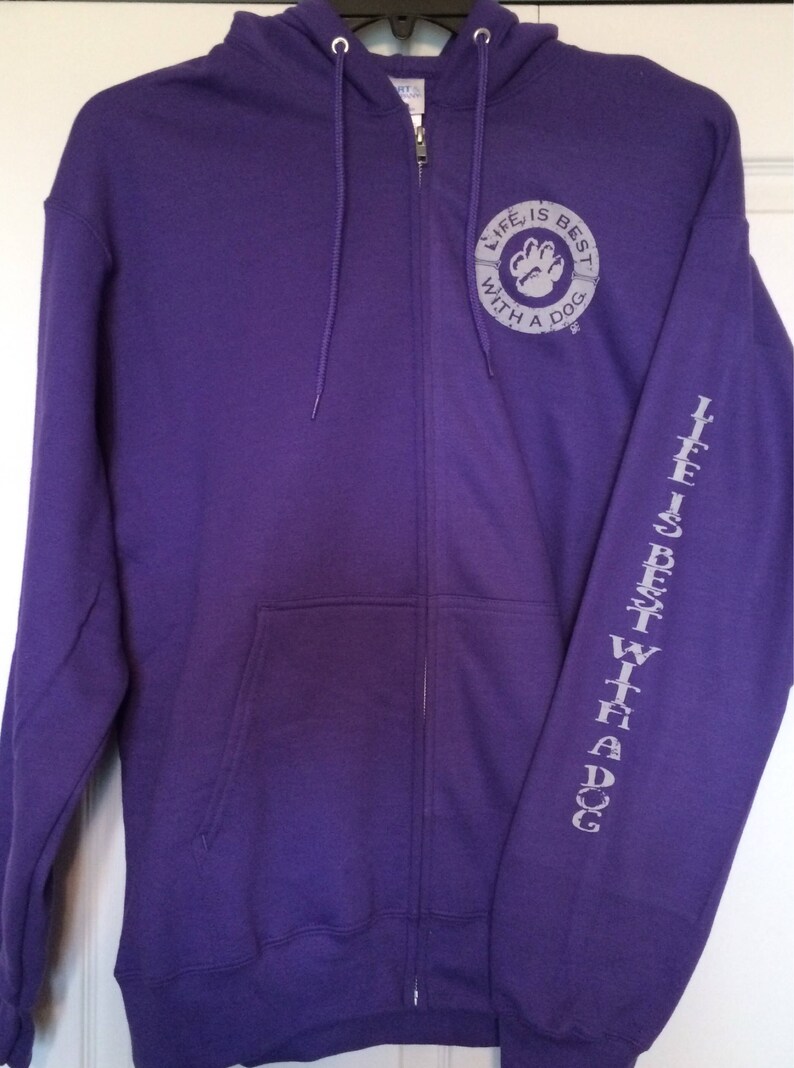 May include: A purple zip-up hoodie with a drawstring hood and front pockets. The left sleeve has the text "LIFE IS BEST WITH A DOG" printed vertically. The chest features a circular design with a paw print and the words "LIFE IS BEST WITH A DOG".