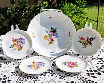 May include: Set of five white porcelain plates with floral designs. The plates feature colorful flowers and leaves in shades of pink, purple, yellow, and green. The plates are perfect for serving desserts, appetizers, or snacks.