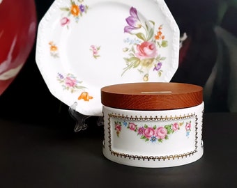 May include: A white porcelain box with a wooden lid and floral designs. The box has a gold trim and is decorated with pink, red, and blue flowers.