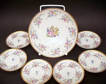 May include: A set of six white porcelain plates with gold trim and floral designs. The plates are arranged in a circle with a larger plate in the center.
