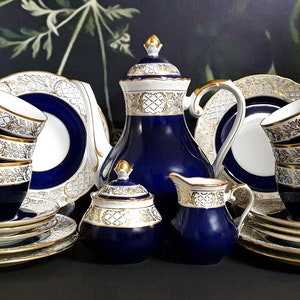 Puede incluir: Un juego de té azul cobalto y dorado con una tetera, una jarra de crema, un azucarero y cuatro tazas y platillos. El juego presenta intrincados detalles dorados y un fondo blanco.