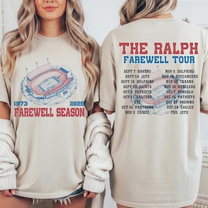 May include: A beige t-shirt featuring a red and blue stadium graphic and the text "1973 Farewell Season 2025." The back of the shirt displays "The Ralph Farewell Tour" and a list of game dates and opponents.