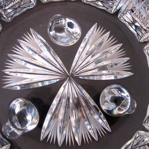 May include: Close-up of a crystal bowl with a cut glass design. The bowl has a starburst pattern in the centre and three round knobs around the edge.