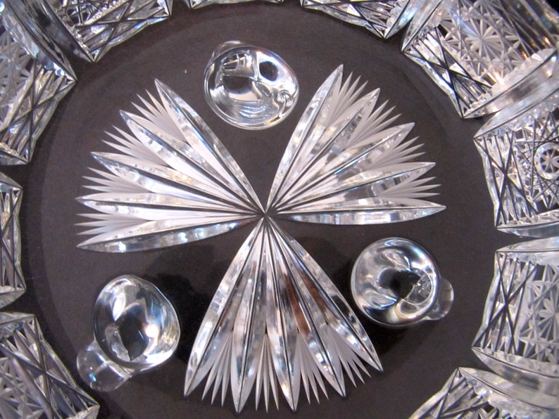 May include: Close-up of a crystal bowl with a cut glass design. The bowl has a starburst pattern in the centre and three round knobs around the edge.